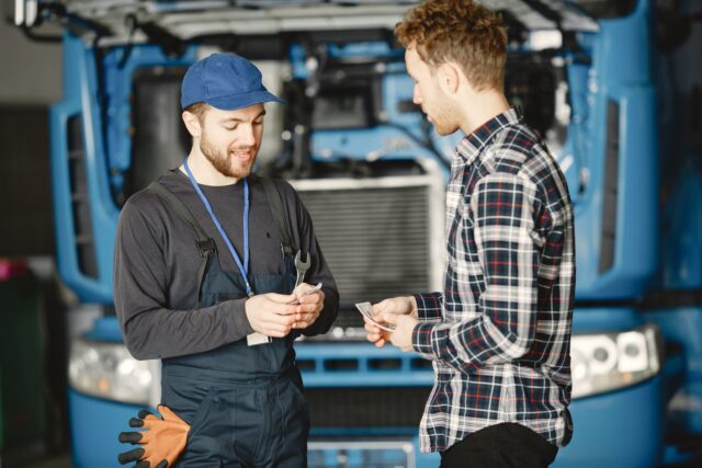 Mecanic care discută cu un client lângă o mașină ridicată pe elevator într-un service auto